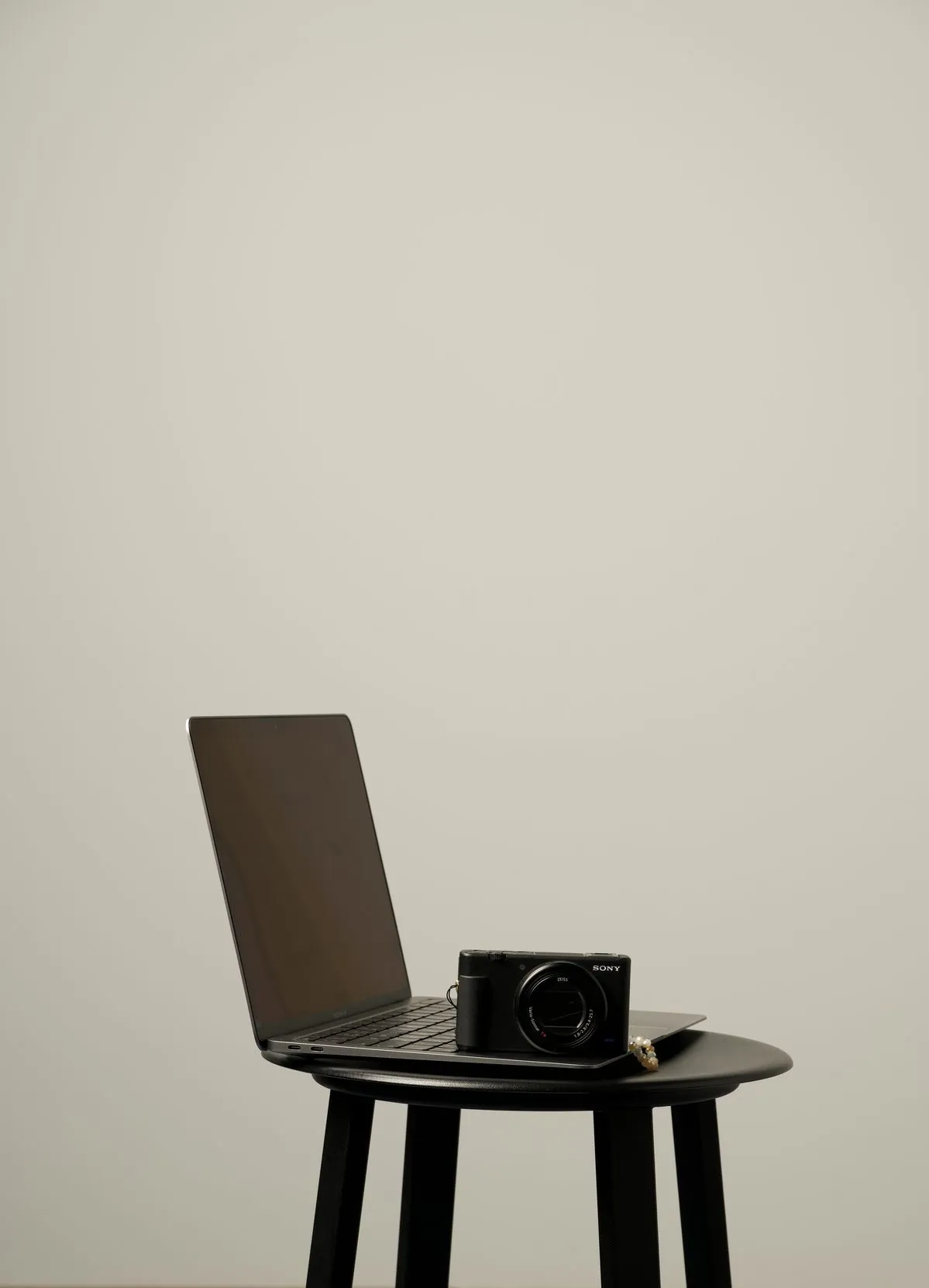 Ordinateur portable et appareil photo Sony posés sur un tabouret noir, fond beige